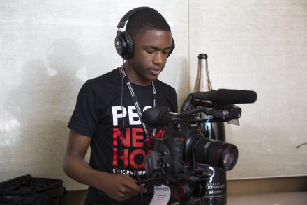 A student stands behind a camera.
