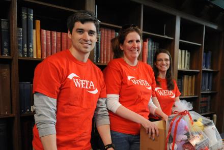 Three volunteers standing behind WETA promotions table t the Folger Shakepeare Library in Washington, D.C.